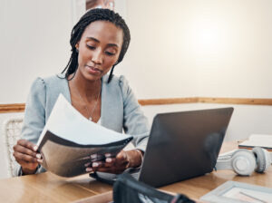 woman looking at paperwork next to laptop on desk